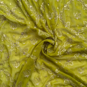 May include: A green fabric with a delicate floral pattern and silver sequins. The fabric is sheer and has a soft, flowing texture.