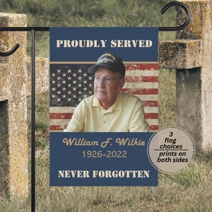 May include: A rectangular garden flag featuring a portrait of an elderly person wearing a military cap against a faded American flag background. Text reads PROUDLY SERVED, William F. Wilkie, 1926-2022, and NEVER FORGOTTEN in gold lettering.