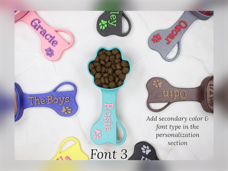 K&ouml;nnte beinhalten: Ein Set aus neun bunten, knochenf&ouml;rmigen Schaufeln f&uuml;r Hunde mit personalisierten Namen. Die Schaufeln sind aus Kunststoff und haben ein Pfotenabdruck-Design. Die Namen auf den Schaufeln sind Gracie, Oscar, ley, Rosie, The Boys, Odin und 12. Die Schaufeln sind in zuf&auml;lliger Reihenfolge auf einer wei&szlig;en Oberfl&auml;che angeordnet. Schriftart 3.