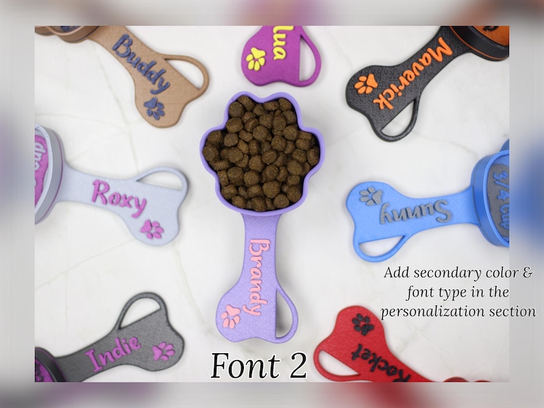 K&ouml;nnte beinhalten: Eine Sammlung von bunten, knochenf&ouml;rmigen Hundefutterl&ouml;ffeln mit Pfotenabdr&uuml;cken und personalisierten Namen, darunter Maverick, Sunny, Brandy, Roxy, Indie, Rocket und Buddy. Die L&ouml;ffel sind aus Kunststoff und haben ein Pfotenabdruckdesign am Griff. Der Text "Font 2" wird unter den L&ouml;ffeln angezeigt.