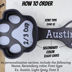 K&ouml;nnte beinhalten: Ein schwarzer und hellgrauer Messbecher in Form einer Pfote mit einem Fassungsverm&ouml;gen von 2/3 Tasse. Der Becher hat einen Griff mit dem Namen "Austin" in wei&szlig;. Der Text "FONT TYPE (FONT 3)" ist &uuml;ber dem Namen sichtbar. Der Text "PRIMARY COLOR (BLACK)" ist &uuml;ber dem Becher sichtbar. Der Text "SECONDARY COLOR (LIGHT GRAY)" ist unter dem Griff sichtbar. Der Text "HOW TO ORDER" ist oben im Bild sichtbar.