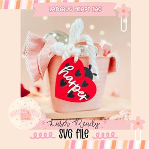 May include: A red ladybug heart tag with the name "harper" in white script. The tag is attached to a pink bucket with a white rope handle. The image also includes the text "Ladybug Heart Tag" and "Laser Ready SVG File".
