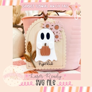May include: A wooden ghost floral arch tag with a white ghost holding a pumpkin. The tag is decorated with pink flowers and gold leaves. The tag says "hymlie" and "Laser Ready SVG File".