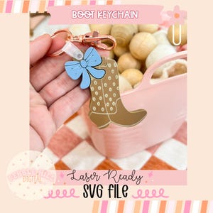 May include: A brown boot keychain with a blue bow and gold polka dots. The keychain is attached to a silver key ring. The text "BOOT KEYCHAIN" is in the upper left corner of the image. The text "Laser Ready SVG FILE" is in the lower centre of the image.