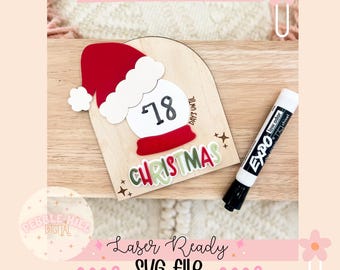 May include: A wooden Christmas countdown sign with a Santa hat and snow globe design. The sign displays "18 DAYS UNTIL CHRISTMAS" and includes the text "CHRISTMAS". An Expo marker is next to the sign. The words "Laser Ready SVG File" are also visible.