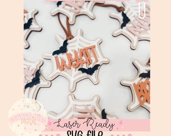 Può includere: Tag a forma di ragnatela con il nome "Wyatt" e ritagli di pipistrelli. I tag sono bianchi, beige e arancioni, con un cordino marrone per appenderli. È visibile anche il testo "Laser Ready SVG File".