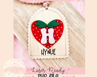 May include: A wooden scallop arch tag with a red heart-shaped strawberry design. The strawberry has white polka dots and a green stem. The letter "H" is in pink and the name "HYNLIE" is written in black below the strawberry. The tag is laser ready and comes as an SVG file.