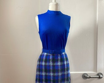 May include: A blue sleeveless top with a high neck and a plaid skirt with a blue, green, and purple pattern. The skirt has a black belt.