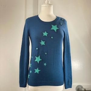 May include: A blue long-sleeved sweater with a pattern of teal stars on the front.