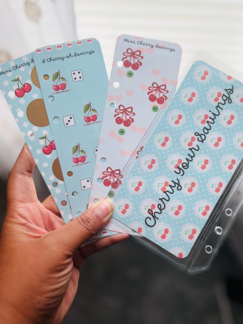 Peut inclure: Ensemble de recharges de planificateur sur le th&egrave;me des cerises. Les recharges pr&eacute;sentent divers motifs, notamment des pois, des d&eacute;s et des illustrations de cerises. Le texte "Mini Cherry Savings" et "Cherry Your Savings" est visible.