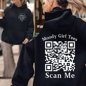 May include: Black hoodie with a white QR code and the text "Moody Girl Tees" and "Scan Me" on the back. The front of the hoodie has the text "Small Business Babe" in a circle.
