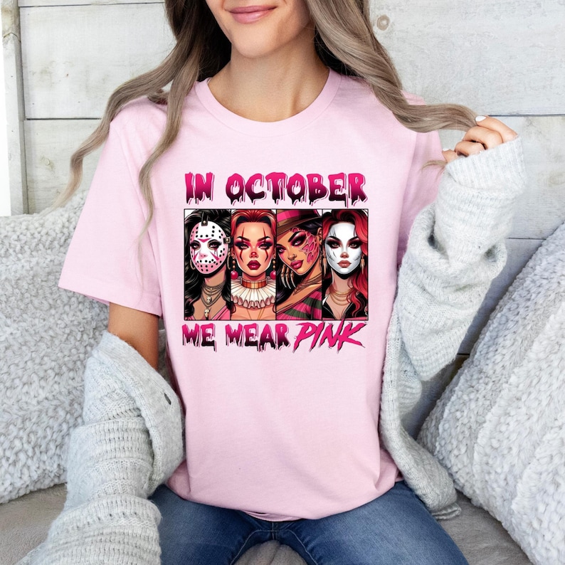 K&ouml;nnte beinhalten: Pinkes T-Shirt mit einem Grafikdruck von vier Frauen, die Halloween-Masken tragen. Der Text "In October We Wear Pink" ist auf dem Shirt aufgedruckt.