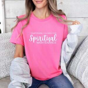May include: A pink t-shirt with the text "Temporarily Closed for Spiritual Maintenance" in white lettering.