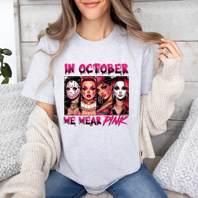 K&ouml;nnte beinhalten: Ein graues T-Shirt mit einem pinkfarbenen Grafikdesign, das vier Frauen zeigt, die Horrorfilm-Masken tragen. Der Text "In October We Wear Pink" ist auf dem Shirt aufgedruckt.