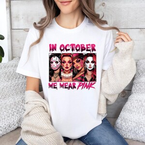 K&ouml;nnte beinhalten: Wei&szlig;es T-Shirt mit einer pinkfarbenen Grafik, auf der "Im Oktober tragen wir Pink" steht. Die Grafik zeigt drei Frauen mit pinkfarbenem und wei&szlig;em Make-up, die Kost&uuml;me tragen.