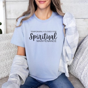 May include: A light blue t-shirt with the text "Temporarily Closed for Spiritual Maintenance" in black.