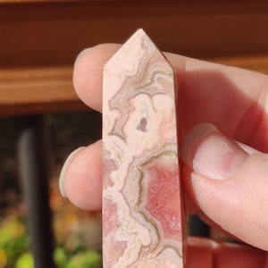 May include: A pink and white banded crystal point, also known as a wand, with a pointed tip and a flat base. The crystal has a natural, rough texture.