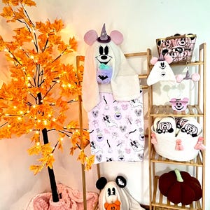 May include: Halloween-themed items, including a hooded towel, blanket, slippers, and decorative basket, all featuring a cartoon mouse design. A plush pumpkin and a decorative tree with orange leaves and lights are also visible.