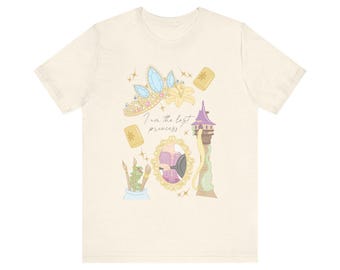 May include: A cream coloured t-shirt with a graphic print of Rapunzel from the Disney movie Tangled. The graphic includes a crown, a chameleon, a frying pan, and the text "I am the lost princess".