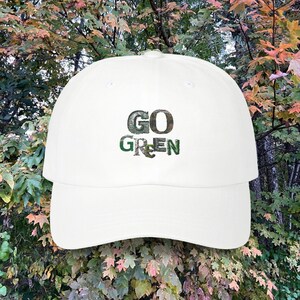Może przedstawiać: Biała czapka bejsbolówka z haftowanym wzorem w kolorze zielonym i czarnym, na którym widnieje napis "GO GREEN".