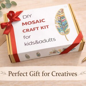 Op de afbeelding: Een doe-het-zelf moza&iuml;ek knutselpakket voor kinderen en volwassenen. De witte doos heeft een rood lint en een kleurrijk veermotief. De tekst op de doos luidt "DIY Mosaic Craft Kit for kids&adults". Een gouden pen ligt op het houten oppervlak.
