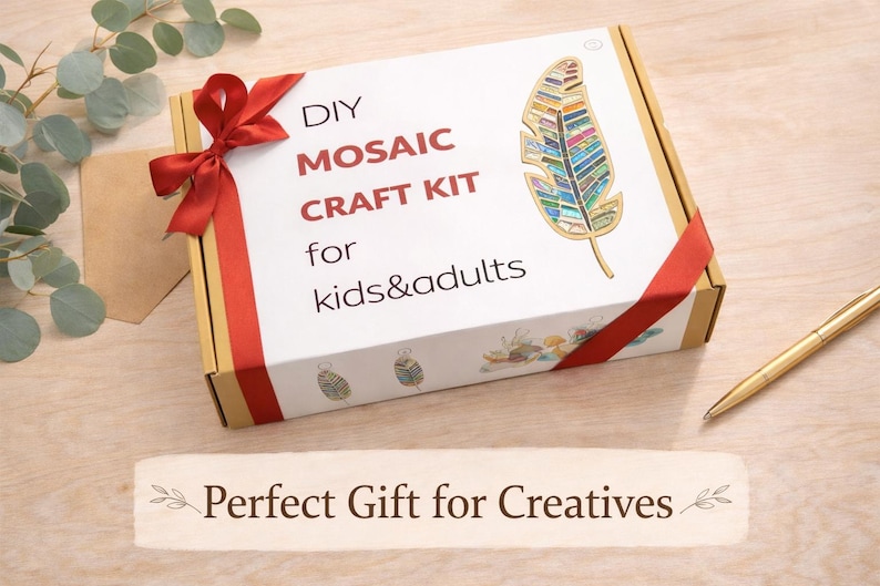 Op de afbeelding: Een doe-het-zelf moza&iuml;ek knutselpakket voor kinderen en volwassenen. De witte doos heeft een rood lint en een kleurrijk veermotief. De tekst op de doos luidt "DIY Mosaic Craft Kit for kids&adults". Een gouden pen ligt op het houten oppervlak.