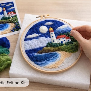 May include: A needle felting kit with a coastal lighthouse scene. The artwork is in a wooden hoop, with a lighthouse, ocean, and beach. The kit includes wool roving in various colors, and the text "DIY Needle Felting Kit".