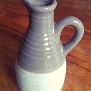 May include: A ceramic jug with a grey top and white bottom. The jug has a rounded body and a handle.