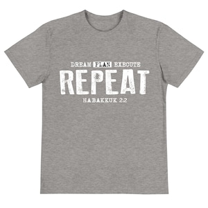 May include: A heather gray t-shirt with the words "DREAM PLAN EXECUTE REPEAT" in a distressed white font. Below the word "REPEAT" is the text "HABAKKUK 2:2". The shirt has a crew neck and short sleeves.