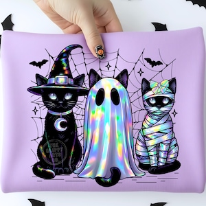 May include: A light purple rectangular pouch featuring a graphic of three black cats. One cat wears a holographic witch hat and crescent moon collar, one is draped in a holographic ghost sheet, and one is wrapped in holographic mummy bandages.