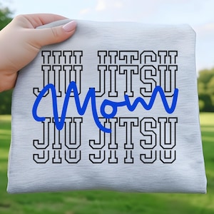 Może przedstawiać: Jasnoszara koszulka z czarnymi słowami "JIU JITSU", ułożonymi w trzech rzędach. Słowo "Mom" jest napisane niebieską kursywą nad środkowym "JIU JITSU". Koszulka jest trzymana przez dłoń.