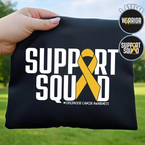 May include: Black tote bag with the words "SUPPORT SQUAD" in white, a yellow ribbon, and the text "#CHILDHOOD CANCER AWARENESS". Two circular designs read "WARRIOR" and "SUPPORT SQUAD" with a yellow ribbon.