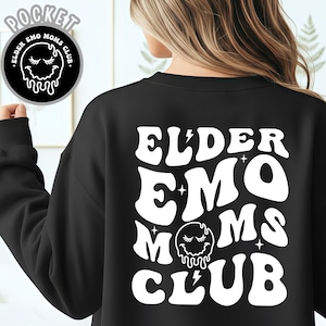 May include: Black sweatshirt with white text that reads "ELDER EMO MOMS CLUB" on the back. A circular graphic with the text "POCKET ELDER EMO MOMS CLUB" is on the upper left. The design features a melting face and lightning bolt.