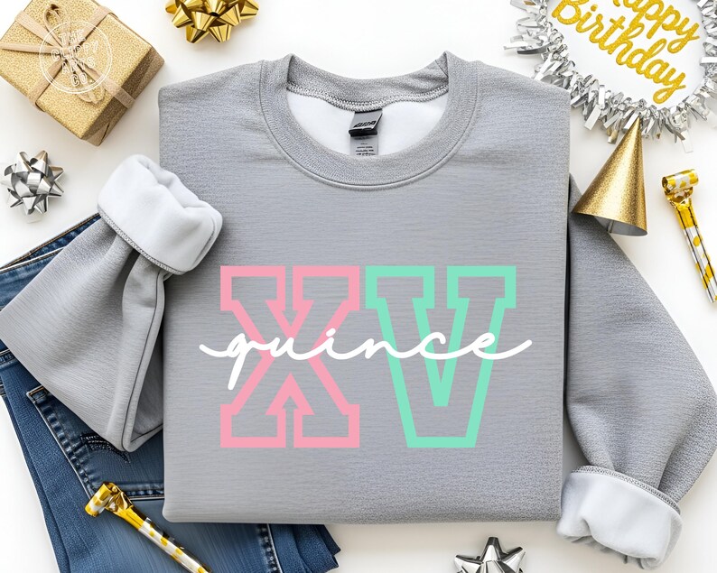 Puede incluir: Una sudadera gris con el texto "XV quince" en letras de bloque rosas y verdes y cursiva blanca. La sudadera tiene pu&ntilde;os blancos y est&aacute; rodeada de decoraciones de cumplea&ntilde;os, incluyendo una caja de regalo dorada y una pancarta de "Happy Birthday".