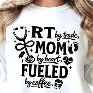 May include: White sweatshirt with a black graphic. The graphic includes a stethoscope, pill, baby footprints, and a coffee cup. Text reads: "RT by trade, MOM by heart, FUELED by coffee."
