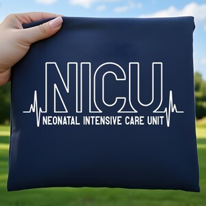 May include: A navy blue pouch featuring the white text "NICU" and "NEONATAL INTENSIVE CARE UNIT" beneath it. A white heartbeat line design flanks the text. The pouch is held by a hand.
