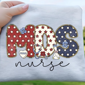 May include: A light gray t-shirt featuring the text "MDS nurse" in a patriotic design. The letters are filled with red, white, and blue stars. A stethoscope, flowers, and a duck wearing a nurse's hat are also included.