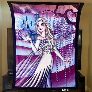 Op de afbeelding: Een zachte deken met een kleurrijke illustratie van een personage uit de animatiefilm Frozen. Het ontwerp toont het personage in een witte jurk tegen een paarse en blauwe achtergrond. De deken heeft een donkerpaarse rand en de tekst "Kat B Treasures".