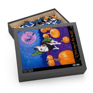 May include: A 120 piece 8x10 inch puzzle featuring a dog dressed as a witch with a green hat and cape. The dog is surrounded by pumpkins and a full moon in the background. The text on the box reads "Which way to the treats?"