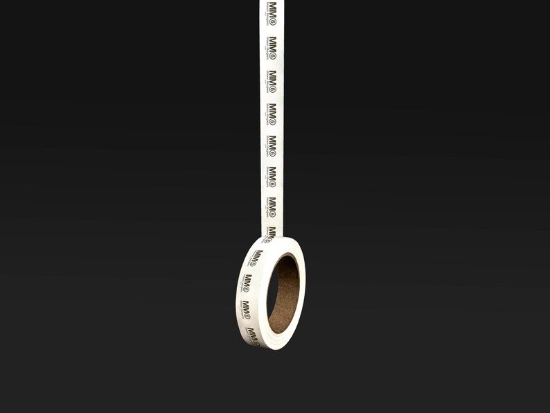 K&ouml;nnte beinhalten: Eine Rolle wei&szlig;es Klebeband mit dem Text "MMD", der sich wiederholt darauf befindet. Das Band befindet sich auf einem schwarzen Hintergrund.