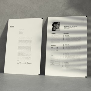 Op de afbeelding: Twee crèmekleurige papieren documenten leunen tegen een grijze muur. Het document rechts is een cv met een foto van een persoon en de naam "Mari Adams". Het document links is een brief. Beide hebben zwarte tekst.