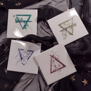 May include: Four white square tiles with black and green floral designs. Each tile features a different floral design within a triangle shape.