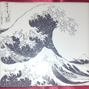 May include: A black and white print of a large wave crashing over three boats. The wave is depicted in great detail, with foamy crests and swirling water. In the background, a mountain peak is visible.