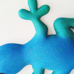 Puede incluir: Una escultura abstracta caprichosa en tonos azules y turquesas, adornada con peque&ntilde;os puntos rosas y amarillos. La obra presenta formas redondeadas y org&aacute;nicas, con dos formas ovaladas oscuras que sugieren ojos. El dise&ntilde;o general evoca una est&eacute;tica l&uacute;dica e imaginativa.