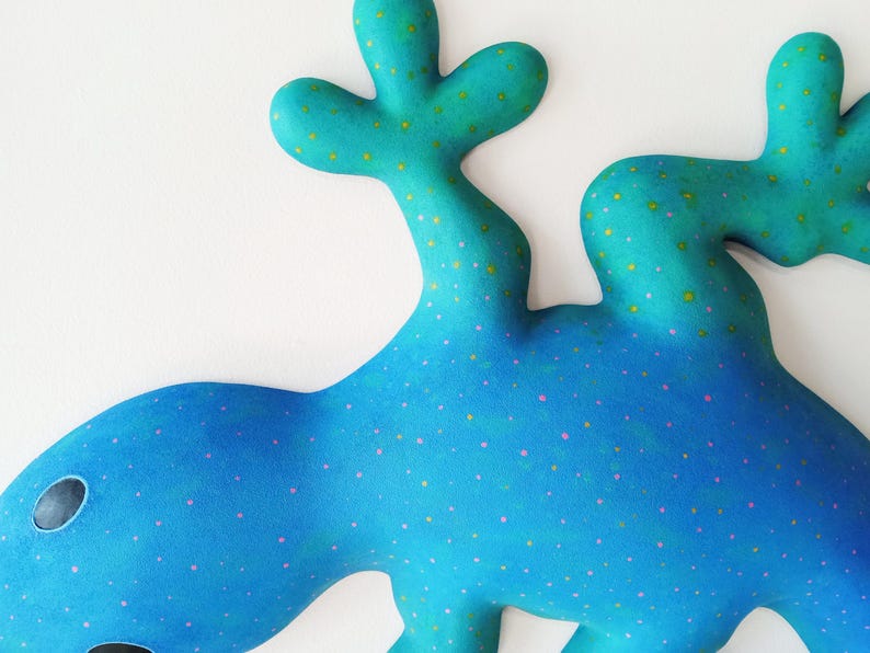 Puede incluir: Una escultura abstracta caprichosa en tonos azules y turquesas, adornada con peque&ntilde;os puntos rosas y amarillos. La obra presenta formas redondeadas y org&aacute;nicas, con dos formas ovaladas oscuras que sugieren ojos. El dise&ntilde;o general evoca una est&eacute;tica l&uacute;dica e imaginativa.