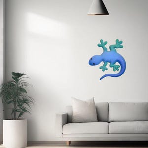 Puede incluir: Decoraci&oacute;n mural de lagarto azul con patas y cola turquesa, montada en una pared blanca. El lagarto es el punto focal, con un dise&ntilde;o interior minimalista que incluye un sof&aacute; gris, una alfombra blanca y una planta en maceta.