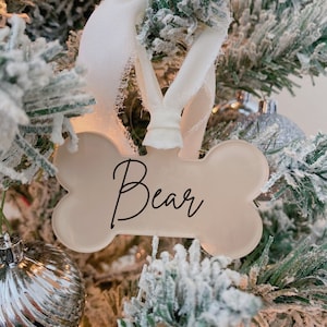 May include: White bone-shaped Christmas ornament with the name "Bear" written in black script.
