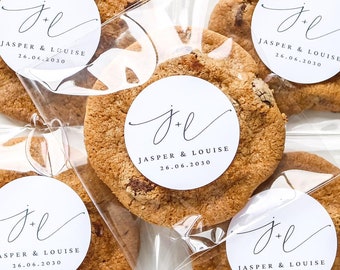 May include: Five individually packaged cookies with a white round sticker on each. The sticker has the initials "J & L" in cursive script and the text "Jasper & Louise 14.04.2019".