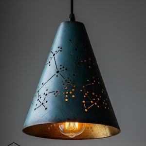 May include: A teal pendant light with a constellation pattern cut into the shade. The interior of the shade is gold, and a vintage-style light bulb is visible. The light hangs from a black cord.