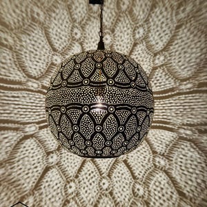 May include: A black, spherical pendant lamp with detailed dot patterns, creating a decorative light pattern on the wall. The lamp is suspended by a chain and emits a warm glow, ideal for ambient lighting in a room.
